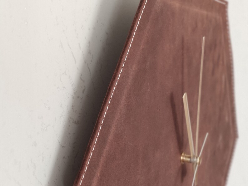 May include: A brown leather clock with white stitching around the edges. The clock face is a hexagon shape and has gold hands.