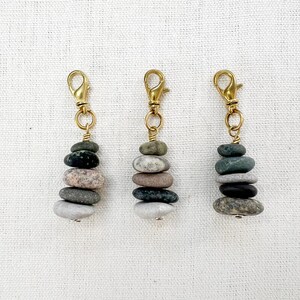 May include: Three keychains, each featuring a stack of small, natural stones in varying colors. The stones are held together with wire and attached to a gold-colored clasp. The keychains are displayed against a neutral background.