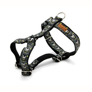 May include: A black and grey dog harness with a repeating pattern of a cartoon superhero. The harness has a black adjustable strap and a silver metal D-ring. The harness has a brown leather tag that says "KENDOG".