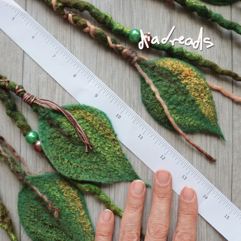 May include: Green felted leaf hair extensions with wrapped yarn and beads, featuring the text "diadreads". A white ruler shows the leaves measure approximately 3 to 4 inches in length, with the entire piece extending past 15 inches in total.