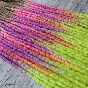 May include: A set of colourful wool dreadlocks with a gradient of pink, purple, orange, yellow, and green. The dreadlocks are made of soft, fluffy wool and are perfect for adding a pop of colour to any hairstyle.
