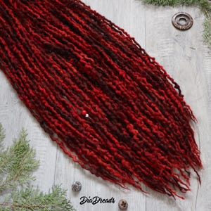 May include: A set of long, red and burgundy wool dreadlocks. The dreadlocks are arranged in a loose, flowing style. The dreadlocks are made of wool and have a natural, textured look.