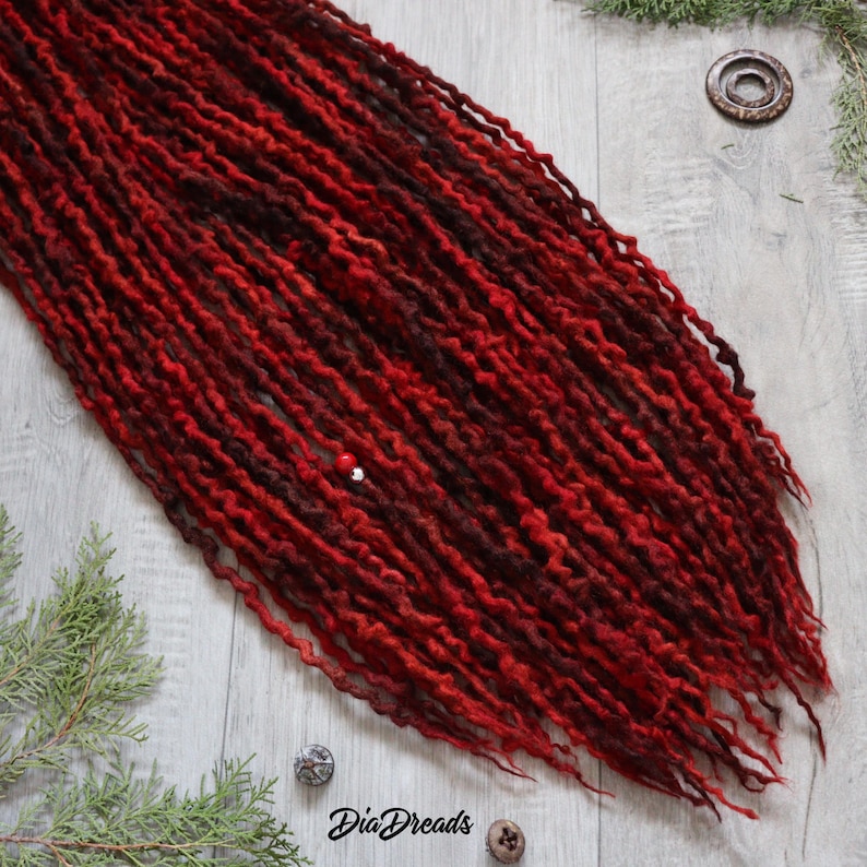 May include: A set of long, red and burgundy wool dreadlocks. The dreadlocks are arranged in a loose, flowing style. The dreadlocks are made of wool and have a natural, textured look.