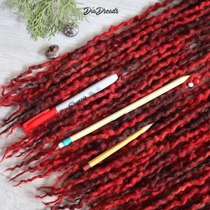May include: Red and brown wool dreadlocks with a red marker and two pencils on a white wooden surface.
