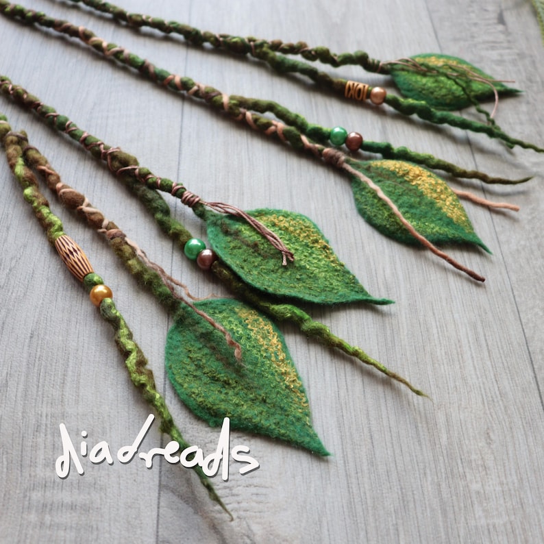May include: Four green and brown felted hair extensions featuring twisted fiber strands, metallic beads, and attached felt leaves with gold accents. The text "diadreads" is visible in white script at the bottom left of the image.