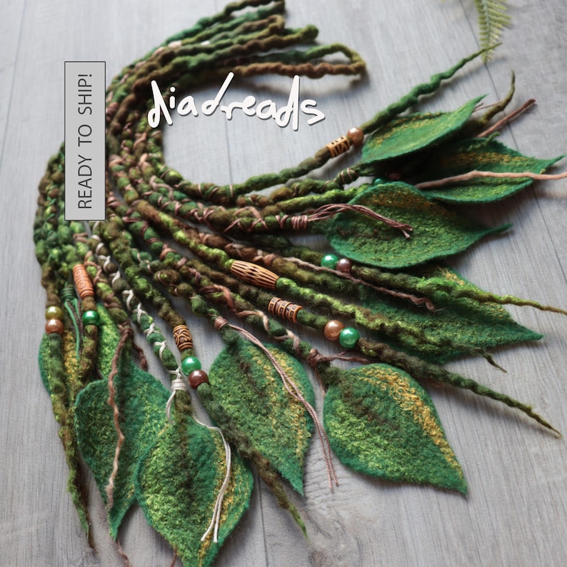 A set of green and brown felted hair dreadlocks featuring attached felt leaves, wooden beads, and metallic accents. The text "diadreads" and "READY TO SHIP!" is visible on the image. The dreadlocks have a textured, twisted appearance.