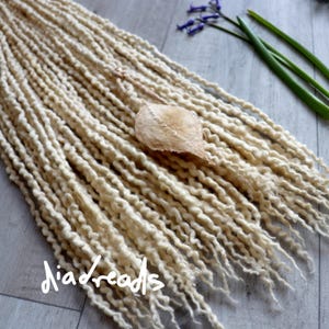 May include: A close-up of a bundle of long, cream-colored wool dreadlocks. The dreadlocks are soft and fluffy, and they are arranged in a loose, flowing style. The dreadlocks are perfect for adding a touch of bohemian chic to any outfit.