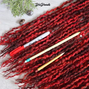 May include: Red and brown wool dreadlocks with a red marker and two pencils on a white wooden surface.