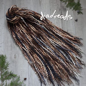 May include: A set of wavy synthetic dreadlocks in a blend of dark brown, light brown, cream, and charcoal gray tones. The dreadlocks are bundled at the top and fan out, featuring the white text "diadreads" written in a script font across the top.