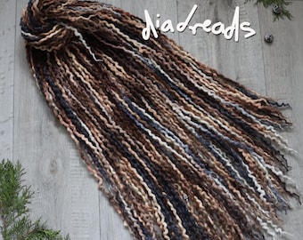 May include: A set of wavy synthetic dreadlocks in a blend of dark brown, light brown, cream, and charcoal gray tones. The dreadlocks are bundled at the top and fan out, featuring the white text "diadreads" written in a script font across the top.