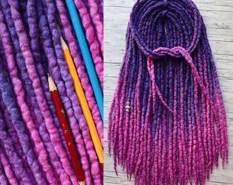 May include: A set of synthetic dreadlocks in a gradient of purple and pink, featuring a textured, wool-like appearance. The dreadlocks are arranged in a bundle with a small silver bead accent. The text Dia Dreads is visible in the top right corner.