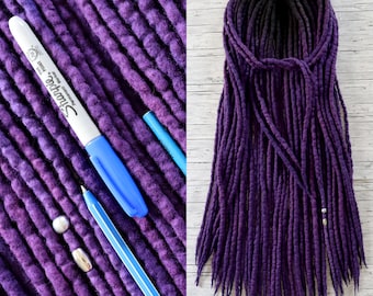 May include: A close-up of purple dreadlocks with a black top, next to a purple fabric with a blue Sharpie marker and pen. The dreadlocks are tied together at the top. The text "DiaDreads" is at the bottom right.