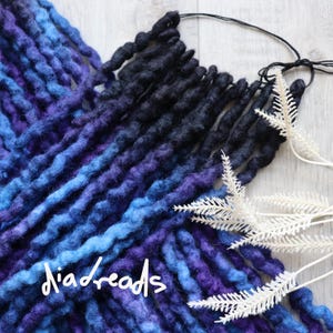 May include: A set of blue and black wool dreadlocks with a gradient from black to blue. The dreadlocks are tied together with a black string.