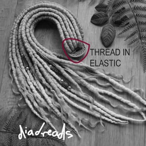 May include: A set of light-colored synthetic dreadlocks featuring a circular elastic band connector. The dreadlocks are adorned with various metallic beads and charms. The image includes the text THREAD IN ELASTIC and the brand name diadreads.