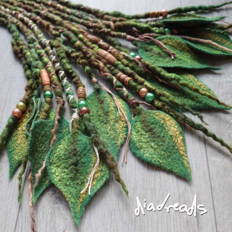 May include: A set of green and brown felted dreadlocks featuring leaf-shaped attachments, wooden and metallic beads, and decorative thread wraps. The text "diadreads" is visible in the bottom right corner of the image.