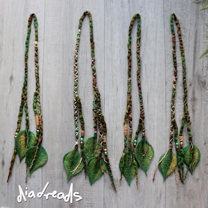 May include: Four sets of green and brown hair extensions featuring felted leaf accents, braided textures, and small wooden and metallic beads. The extensions are arranged vertically, and the text "diadreads" is visible in the bottom left corner.