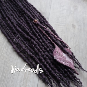 May include: Dark purple dreadlocks with a decorative leaf accent and a small bead. The dreadlocks are arranged diagonally across the frame. The text "diadreads" is written in white script at the bottom left.