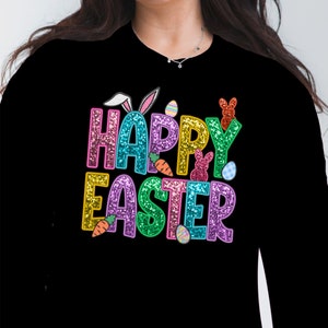 May include: A black long-sleeved shirt with a colorful glittery "Happy Easter" design. The design includes a bunny, carrots, and Easter eggs.