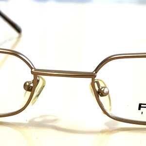 May include: A pair of gold-toned metal eyeglasses with a rectangular frame. The brand name "PEZZO ITALY" is printed on the right lens.