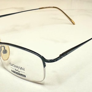 Könnte beinhalten: Schwarz-goldfarbene Brille mit rechteckigem Rahmen und Halbrand-Design. Die Brille trägt den Text "GIOVANNI Italy EYEWEAR" auf dem Glas. Die Bügel sind dünn und gehen in goldfarbene Ohrenteile über.