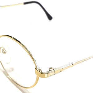 Könnte beinhalten: Goldfarbene runde Brille mit dünnen Metallrahmen und klaren Gläsern.