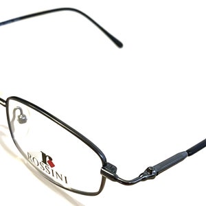 Pode incluir: Óculos de metal preto com armação e lentes transparentes. O nome da marca "ROSSINI" está impresso na armação.