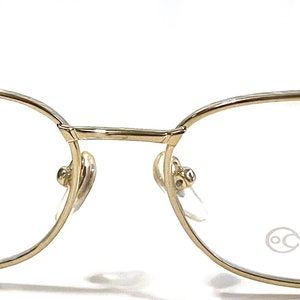 Könnte beinhalten: Goldfarbene rechteckige Metallbrille mit klaren Gläsern. Das rechte Glas trägt den Schriftzug "FOCUSSS".