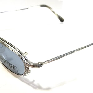 Può includere: Occhiali da sole in metallo argentato con lenti blu. Gli occhiali hanno una montatura sottile e delicata e un design semplice.