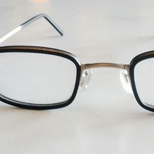 Pode incluir: Óculos retangulares com armação preta e hastes prateadas. As lentes transparentes exibem a marca "BOSS". Uma etiqueta preta com o logotipo "BOSS" está presa à armação.