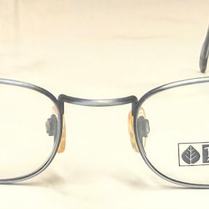 May include: Oval-shaped eyeglasses with a thin, dark blue metal frame. The lenses are clear, and the nose bridge is a darker shade of blue. The temples curve and have a dark blue finish. The brand name "Daniel Hunter Aspen Colorado" is printed on the right lens.