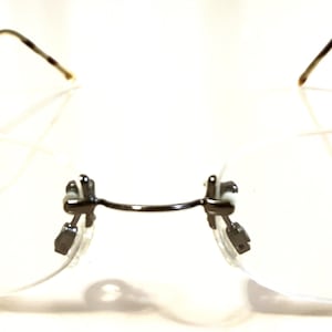 May include: Silver rimless glasses with a clear frame and a DR logo on the right temple. The logo reads "DR No. 1462".