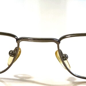 May include: A pair of silver-toned metal spectacles with a rectangular frame and clear lenses. The brand name "Jia B" is printed on the right lens.