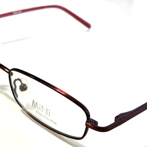May include: Brown metal eyeglasses with red temple arms. The glasses have a rectangular frame and say "Mini Kids Collection" on the side.