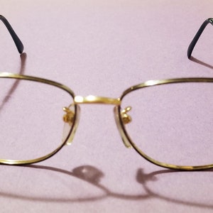 Op de afbeelding: Gouden metalen bril met een rechthoekig montuur en groene pootjes.