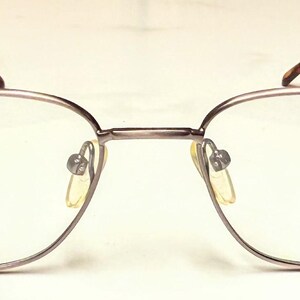 May include: Eyeglasses with a silver metal frame and clear lenses. The arms are dark brown. The brand name "I-VISION EYEWEAR" is printed on the right lens. A classic eyewear design.