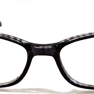 May include: Grey and black eyeglasses with a Star logo on the right lens. The frame is made of plastic and has a rectangular shape. The text "ST-207 52□18" is printed on the left lens.