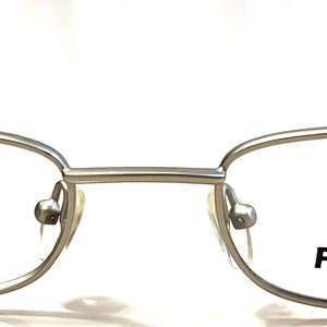 May include: Silver-toned rectangular eyeglasses with the brand name "PEZZO" printed on the right lens.
