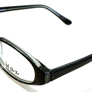 Könnte beinhalten: Schwarze und graue ovale Brille mit dem Wort "Max" auf der rechten Linse.