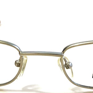May include: Silver-toned metal rectangular eyeglasses with a thin frame and the brand name "PEZZO ITALY" printed on the right lens.