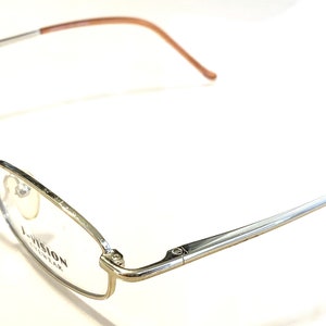 May include: Silver-toned metal eyeglasses with brown plastic temple tips. The glasses have a rectangular frame and the brand name "VISION" is printed on the right lens.