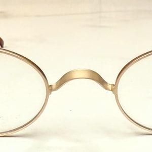 Può includere: Occhiali ovali color oro con lenti trasparenti. Le montature presentano un ponte e aste con un motivo tartarugato. Il testo "Revolutionary Flex Hinge" e "RODENSTOCK" è stampato sulle lenti.