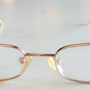 May include: Gold-toned metal eyeglasses with oval lenses. The frames have a delicate, thin design with a bridge and nose pads. The text "UNIQUE COLLECTION" is visible on the lens. The temples are angled and extend to the ear pieces.