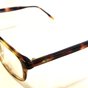 May include: Tortoiseshell eyeglasses with a gold logo on the right temple.