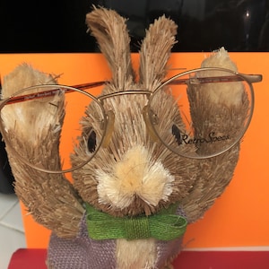 May include: A brown and tan bunny figurine wearing a green bow tie and gold-rimmed glasses with the text "Retro Specs" on the right lens.