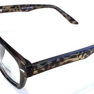 Könnte beinhalten: Braune und schwarze Schildpatt-Brille mit klaren Gläsern. Die Brille hat einen rechteckigen Rahmen und ein dezentes Leopardenmuster.