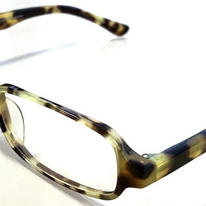 May include: Tortoise shell eyeglasses with a rectangular frame and clear lenses. The arms of the glasses are also tortoise shell.