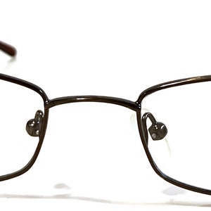 May include: A pair of brown metal eyeglasses with a rectangular frame. The brand name "ROSSINI" is printed on the right lens.