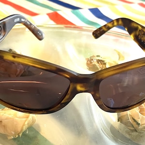 May include: Brown tortoise shell sunglasses with brown lenses. The sunglasses have the word "GUESS" printed on the side.