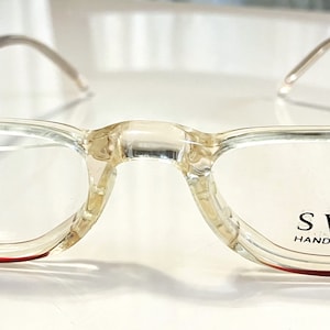 May include: Clear plastic spectacles with a red frame and the text "SWANK HANDMADE IN FRANCE" on the right lens.