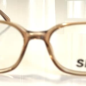 May include: A pair of eyeglasses with a light brown frame and clear lenses. The glasses have a rectangular shape with rounded edges. The text "SMS" is printed on the right lens.